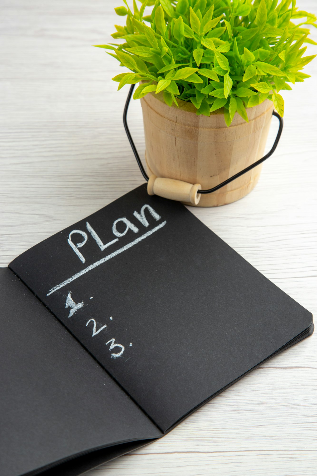 front view dark notepad with plan written list and plant on white background drawing office work